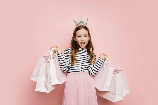 Aufgeregt preteen Mädchen mit Krone Stirnband hält Einkaufstaschen auf rosa Hintergrund — Stockfoto