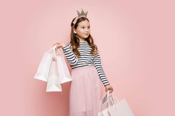 Menina pré-adolescente com cabeça coroa segurando compras no fundo rosa — Fotografia de Stock