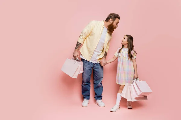Татуированный мужчина держит за руку дочь с покупками на розовом фоне — стоковое фото