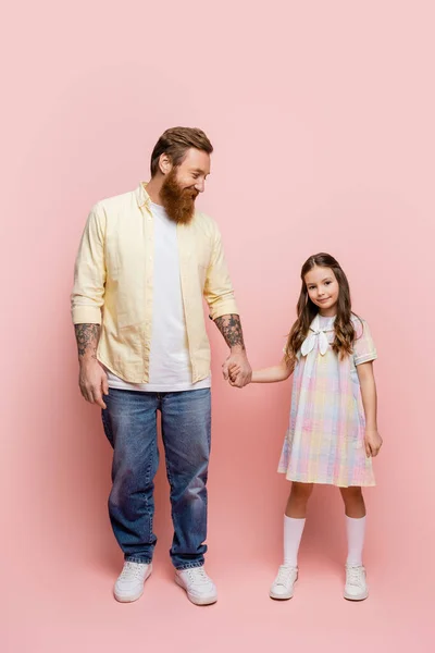 Full length of tattooed man holding hand of preteen daughter on pink background — Stock Photo