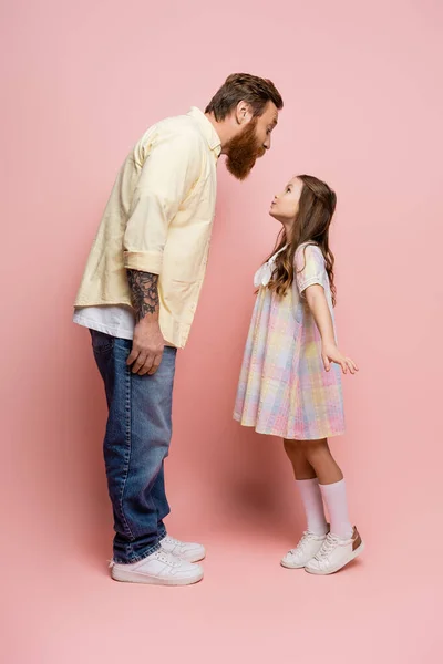 Vista lateral do pai e da filha amuando lábios no fundo rosa — Fotografia de Stock