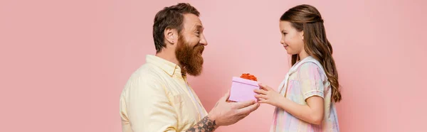 Seitenansicht tätowierter Vater, der Tochter ein Geschenk macht, isoliert auf rosa, Banner — Stockfoto