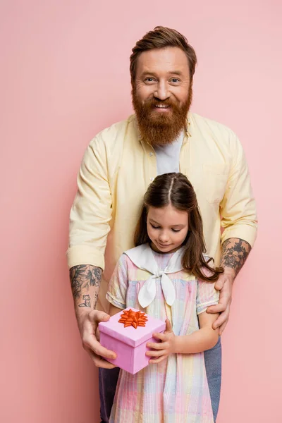 Беззаботный человек дарит подарок дочери-подростку на розовом фоне — стоковое фото