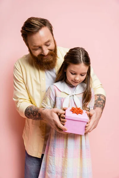 Tattooed man holding gift near preteen daughter on pink background — Stock Photo