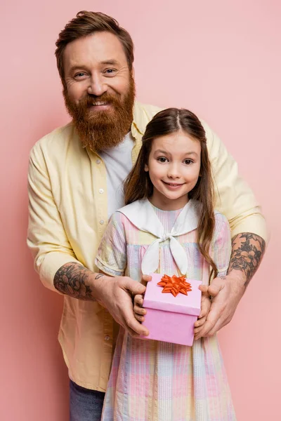 Homme tatoué positif tenant boîte cadeau près de la fille sur fond rose — Photo de stock