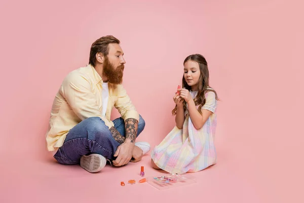 Preteen girl holding lipstick near tattooed dad on pink background — Stock Photo