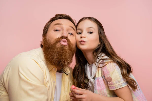 Preadolescente niño sosteniendo lápiz labial y pucheros labios cerca de padre aislado en rosa - foto de stock