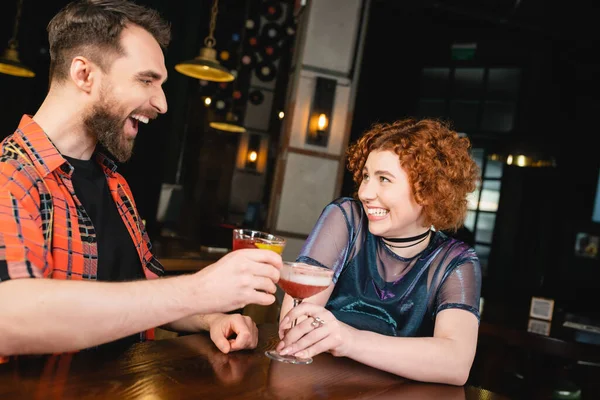 Lächelnde Freunde klappern kalte Cocktails in der Nähe des Holzstandes in der Bar — Stockfoto