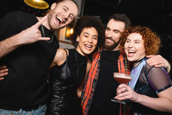 Захоплена жінка тримає конюшню клубний коктейль біля безтурботних міжрасових друзів дивлячись на камеру в барі — стокове фото