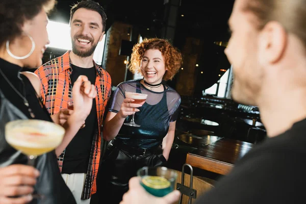 Amis multiethniques positifs avec différents cocktails se réunissant au bar la nuit — Photo de stock
