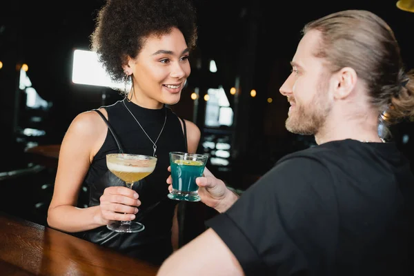 Усміхнена афроамериканська жінка тримає піско кислий коктейль біля розмитого друга в барі — стокове фото