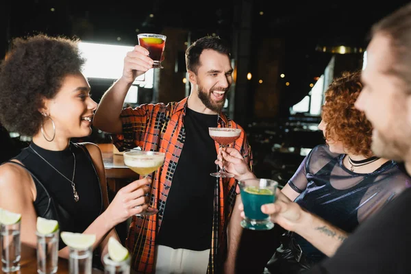 Sorgloser bärtiger Mann hält Negroni-Cocktail neben multiethnischen Freunden in Bar — Stockfoto