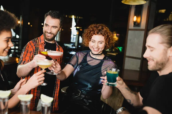 Sourire rousse femme cliquetis cocktails avec des amis multiethniques dans le bar — Photo de stock