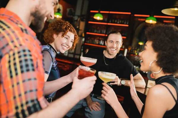 Des gens joyeux regardant un ami afro-américain avec un cocktail parlant au bar — Photo de stock