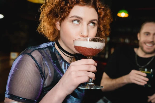 Молодая рыжая женщина пьет коктейль из пены в баре — стоковое фото
