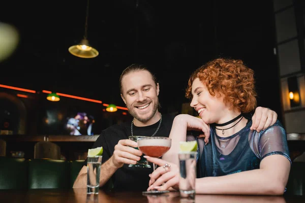 Amis positifs clinking cocktails près de tequila shots avec du citron vert frais dans le bar — Photo de stock