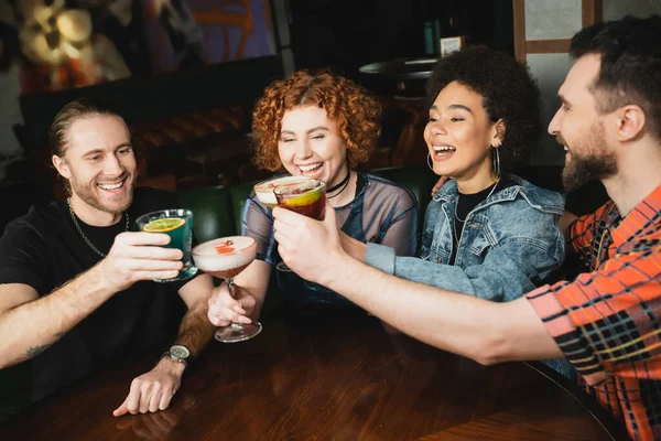 Cheerful multiethnic people clinking different cocktails in bar at night — Stock Photo