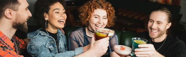 Personas multiétnicas positivas celebrando diferentes cócteles mientras tintinean en el bar, pancarta - foto de stock