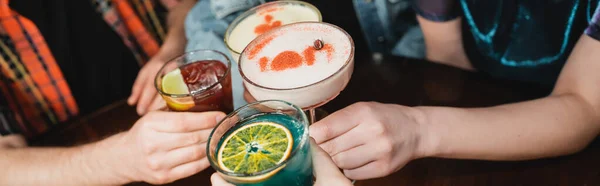 Vista recortada de los jóvenes amigos tintineo con cócteles en el bar por la noche, pancarta - foto de stock