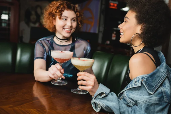 Cheerful interracial friends holding clover club and pisco sour cocktails in bar — Stock Photo