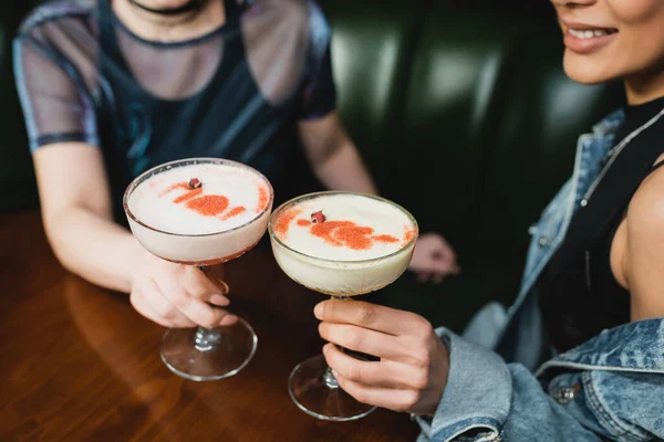 Vue recadrée de copines interracial tenant des cocktails en mousse dans le bar — Photo de stock