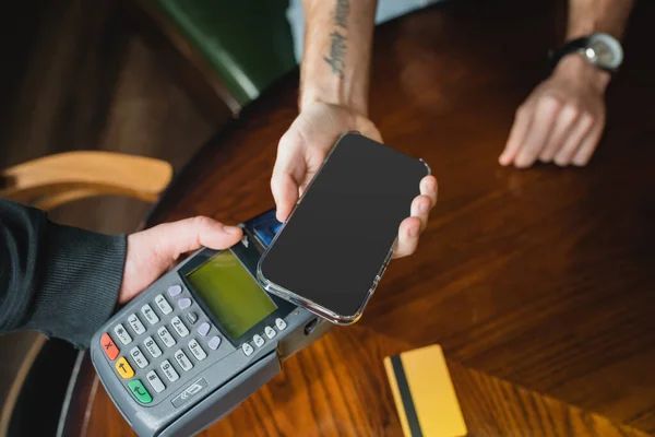 Обрізаний вид чоловіка, який платить зі смартфоном біля офіціанта з платіжним терміналом в барі — стокове фото