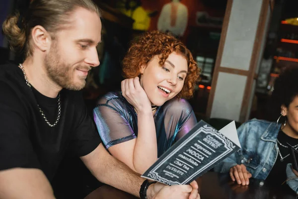 Amigos sonrientes mirando el menú mientras se reúnen en el bar por la noche - foto de stock