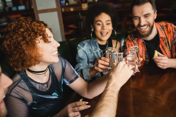 Positive multiethnic friends holding tequila shots with salt and lime in bar — Stock Photo