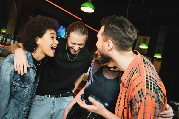 Amigos interracial positivos en ropa casual abrazándose y divirtiéndose en el bar - foto de stock