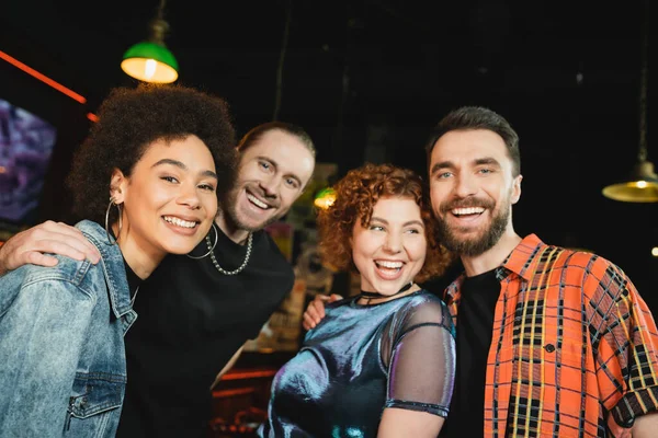 Cheerful interracial people in casual clothes looking at camera in bar at night — Stock Photo