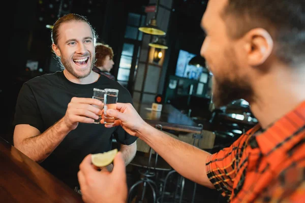 Homme barbu souriant cliquetis tirs de tequila avec un ami flou dans le bar — Photo de stock