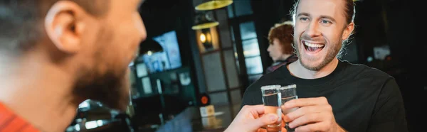 Захоплений чоловік клінкінг текіли з розмитим другом в барі, банер — стокове фото