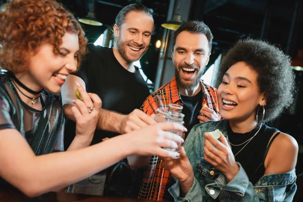 Amigos multiétnicos despreocupados sosteniendo lima y tequila con sal en el bar - foto de stock