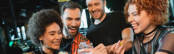 Веселые межрасовые друзья, держащие текилу с солью в баре, баннер — стоковое фото