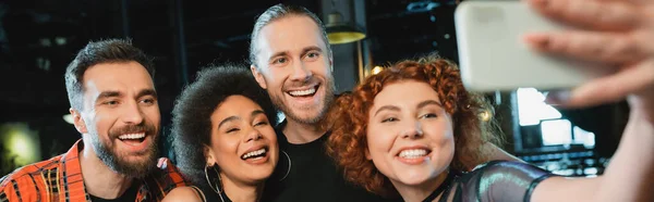 Young redhead woman taking selfie with interracial friends in bar, banner — Stock Photo