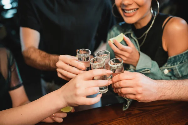 Обрезанный вид мультиэтнических людей, держащих текилу выстрелы с солью на стаканах в баре — стоковое фото