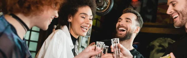 Gente interracial alegre sosteniendo tiros de tequila con sal en el bar, pancarta - foto de stock