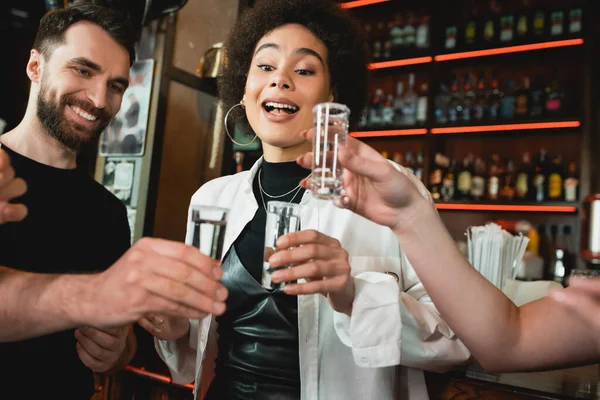 Femme afro-américaine excitée tenant un tir de tequila avec du sel près d'amis dans un bar — Photo de stock