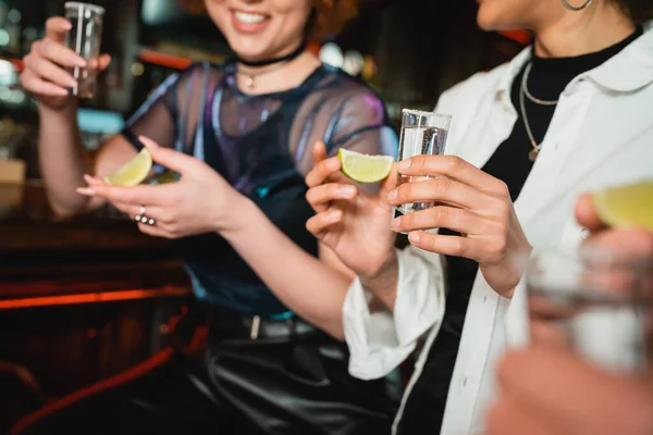 Обрезанный вид улыбающихся мультиэтнических женщин с текилой и лаймом в баре — стоковое фото