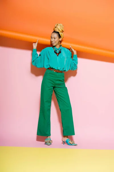 Longitud completa de la mujer afroamericana de moda en traje de verano sonriendo sobre fondo colorido - foto de stock