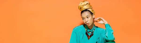 Fashionable african american woman with headscarf touching earring on orange background, banner — Stock Photo