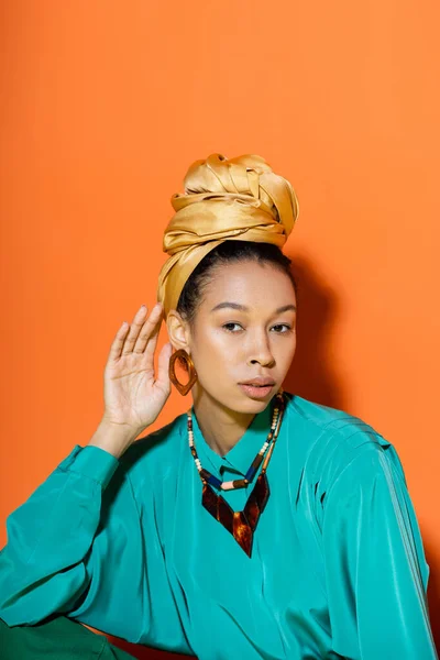 Retrato de mulher americana africana elegante ajustando lenço de cabeça no fundo laranja — Fotografia de Stock