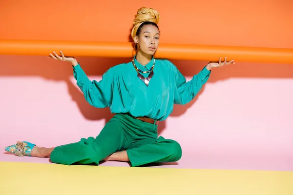 Trendy giovane modello afroamericano in abito estivo seduto su sfondo colorato — Foto stock