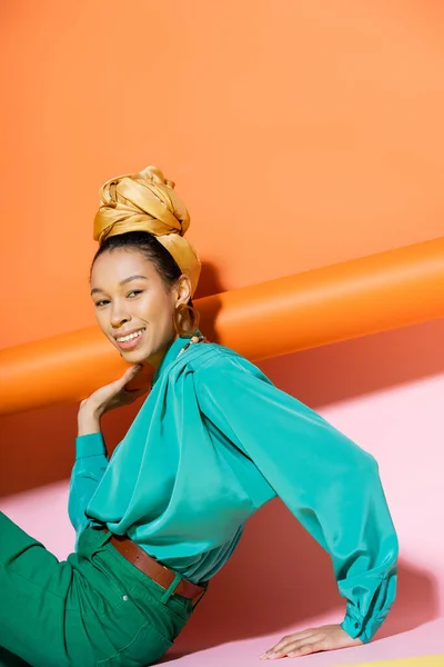 Overjoyed donna afro-americana in abiti estivi seduto su sfondo colorato — Foto stock