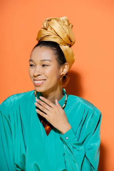 Retrato de modelo afroamericano alegre en pañuelo para la cabeza mirando hacia otro lado sobre fondo naranja - foto de stock