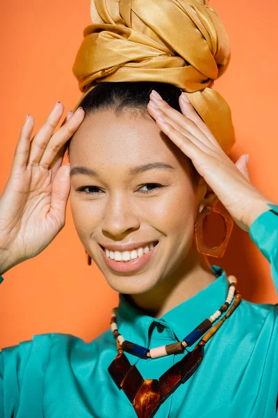 Retrato de la mujer afroamericana de moda en ropa de verano tocando el pelo sobre fondo naranja - foto de stock