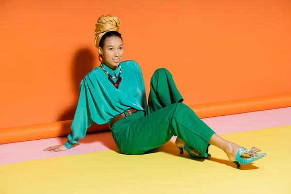 Mulher afro-americana positiva em roupas de verão e sapatos sentados em fundo colorido — Fotografia de Stock