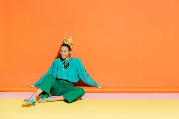 Despreocupado modelo afroamericano en ropa de verano sentado sobre fondo colorido - foto de stock