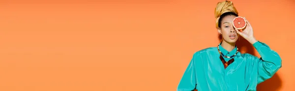 Fashionable african american woman holding grapefruit on orange background, banner — Stock Photo