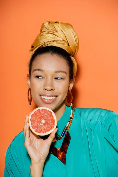 Retrato de sorridente e bem vestido modelo afro-americano segurando toranja em fundo laranja — Fotografia de Stock